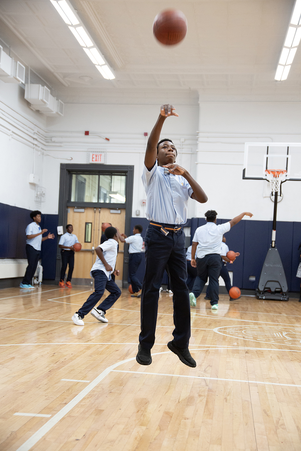 boy in school uniform with tie shoots basketball during drills in gym