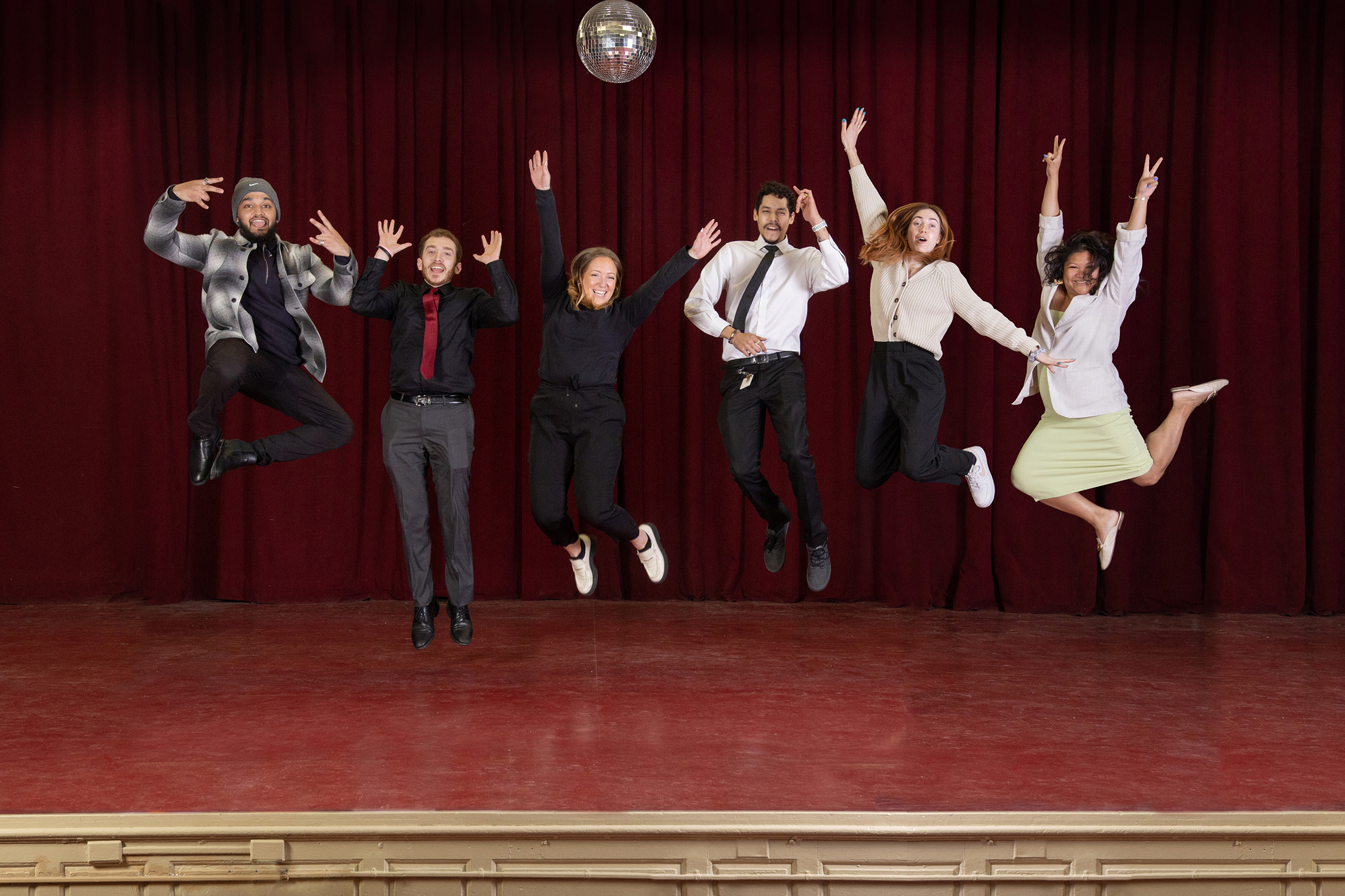 operations associates jump on stage in front of red curtain