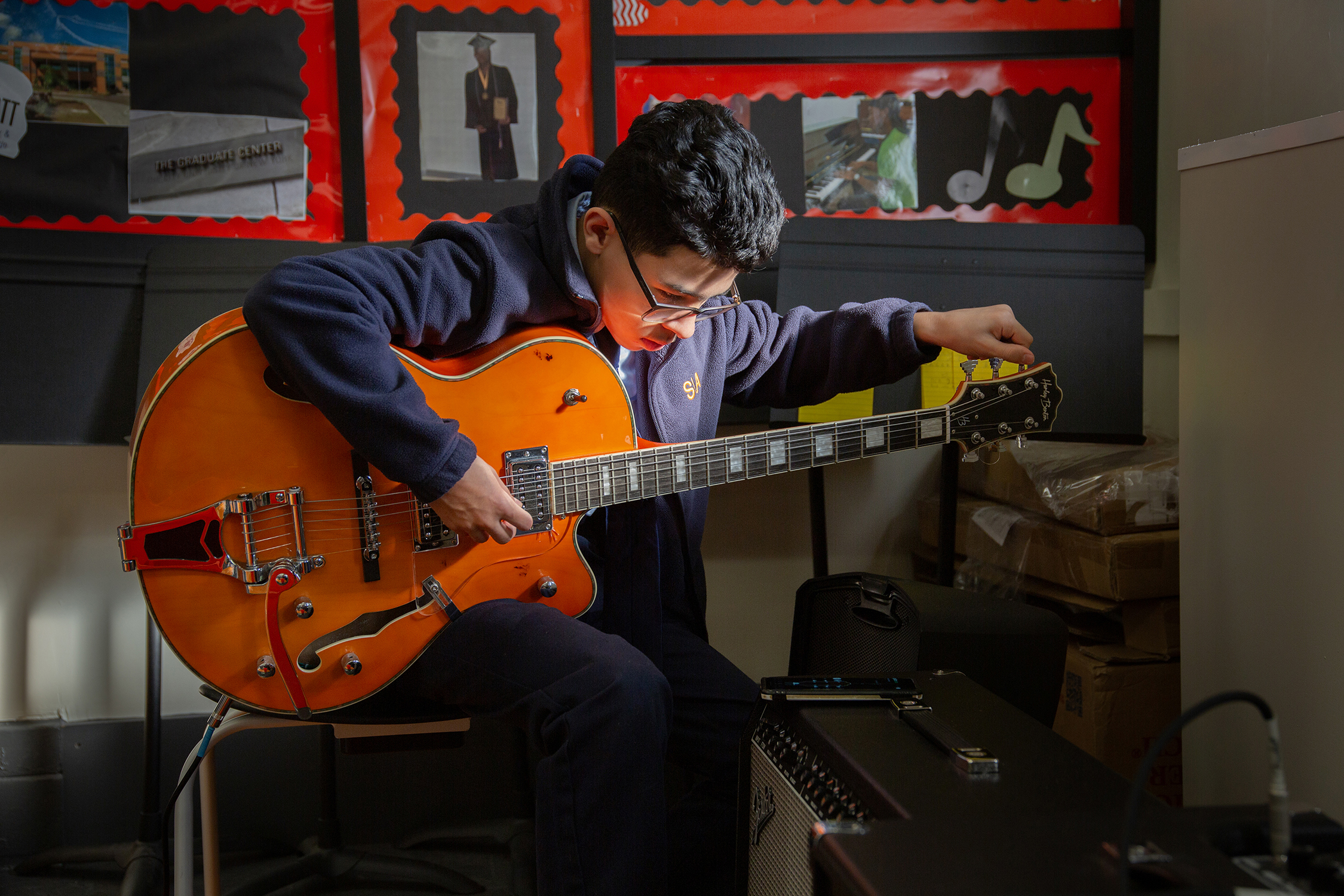 sunlight illuminates a scholar tuning guitar strings before a music club practice at East Flatbush middle school